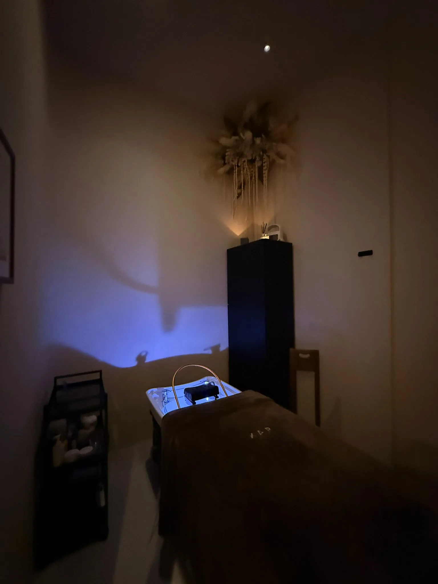 The head spa room at XAR Beauty: the lit basin at the head of the bed, a XAR towel folded on top, candlelight on the wall