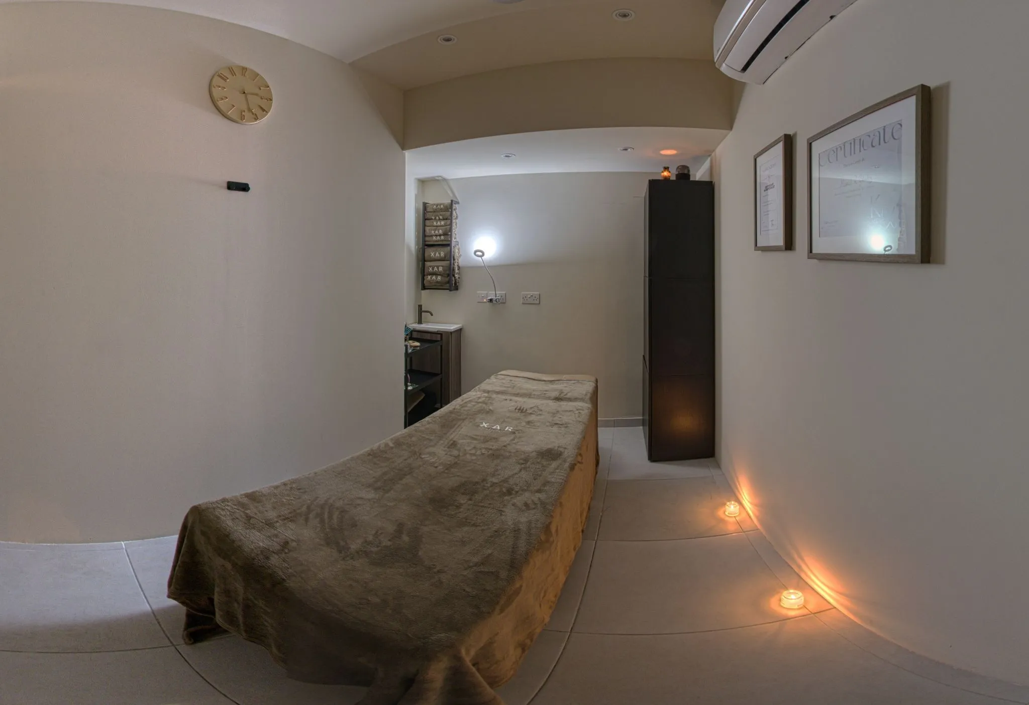 A treatment room at XAR Beauty, lit by candles, with the bed made up in XAR’s own towels